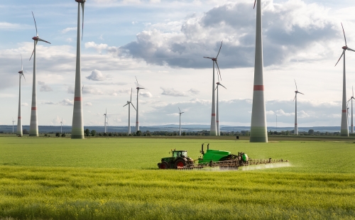 Tractor in agricultural field beneath wind turbines